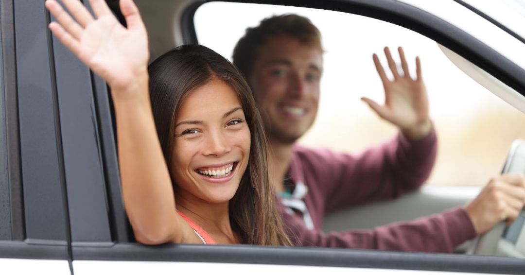 young couple on a road trip waving out the window