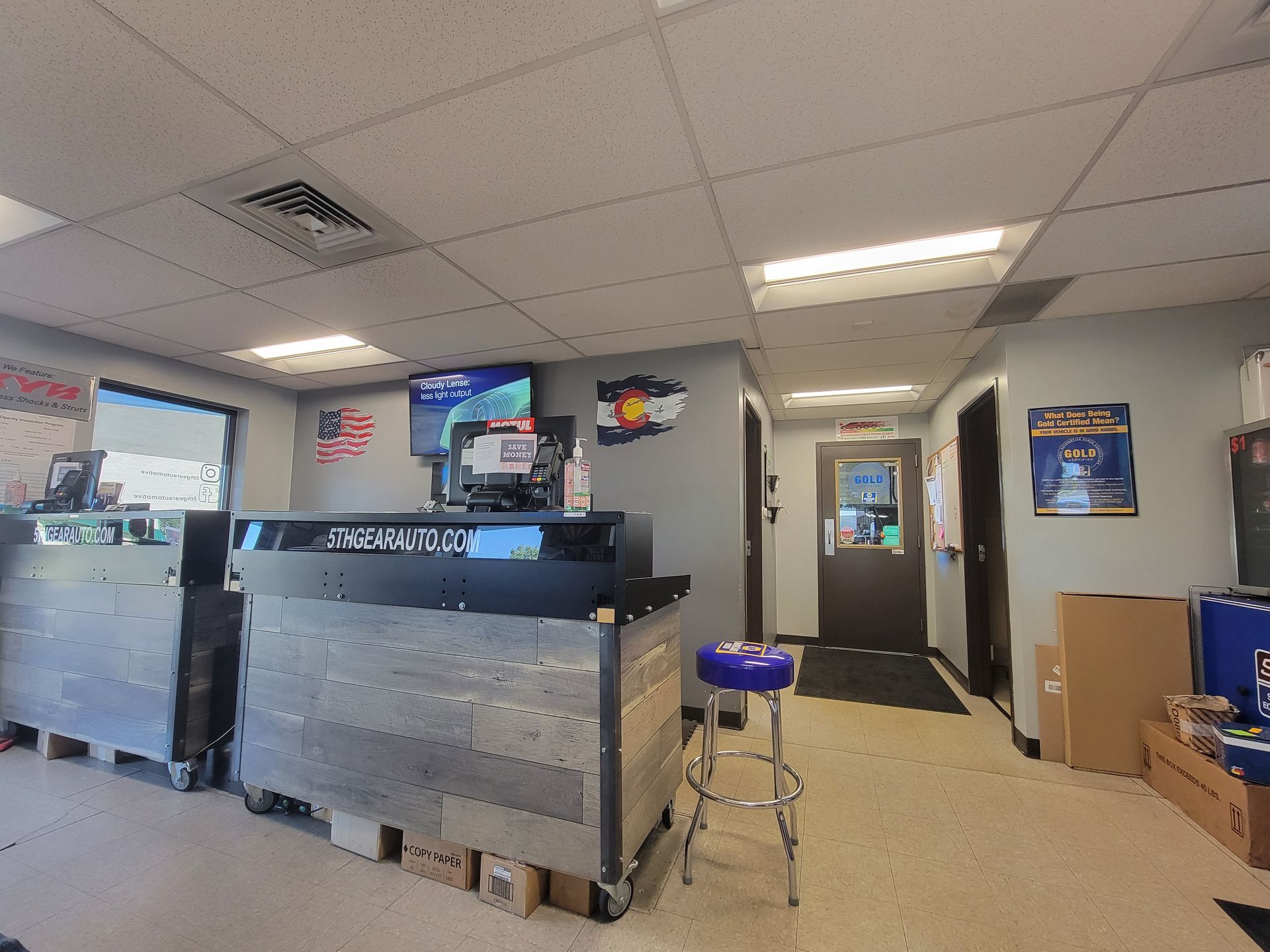 Interior of a car repair shop: front desk with a blue stool, Colorado flag, and a hallway leading to a door. | 5th Gear Automotive