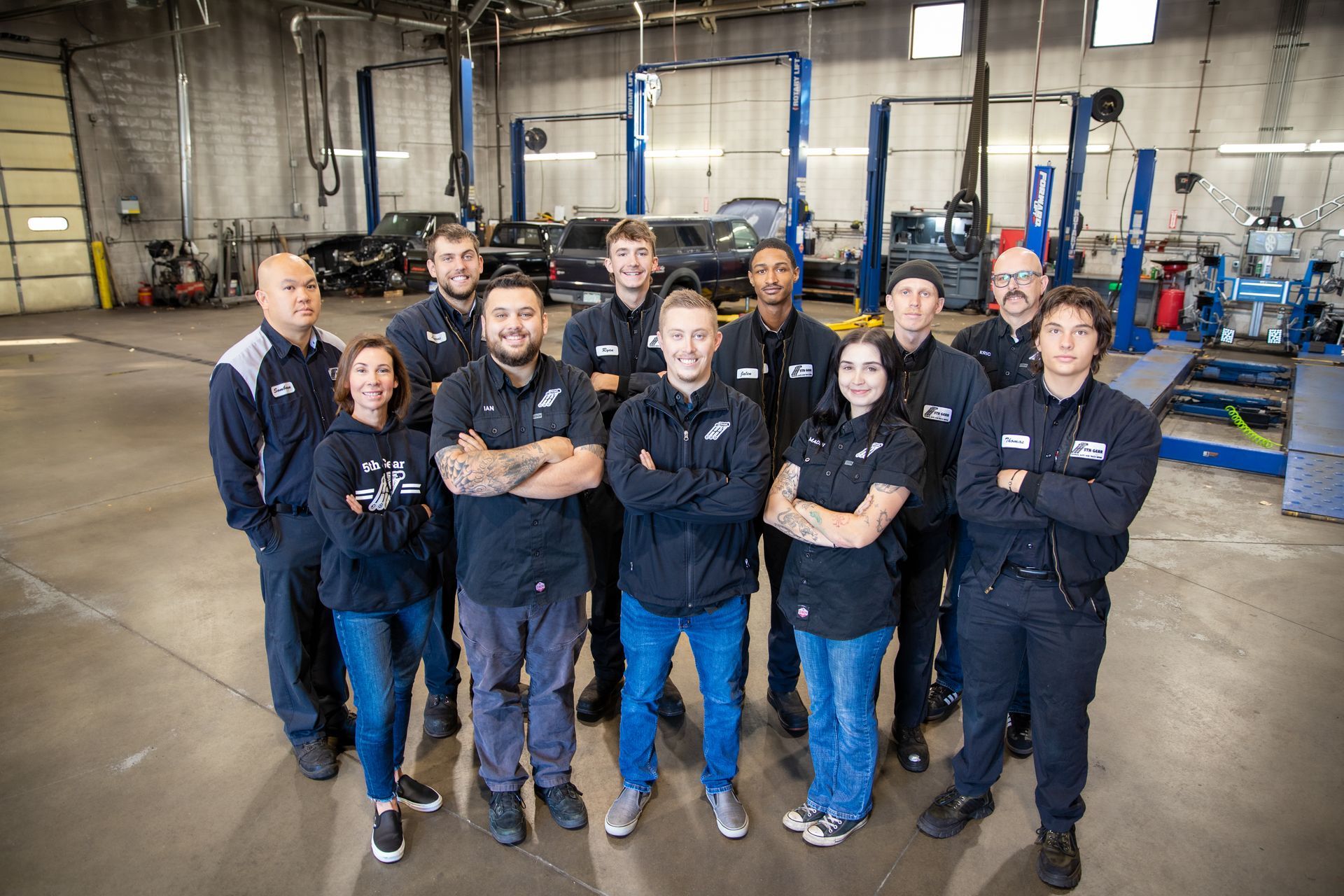 Group of auto shop employees pose together in the garage, arms crossed. | 5th Gear Automotive