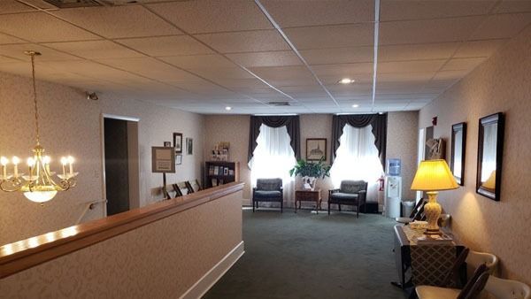 Waiting room with dark green carpet, tan walls, dark curtains, chairs, and a water cooler.