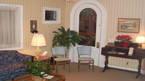 Waiting area with blue patterned sofa, chairs, and potted plants, near a doorway and lamp.