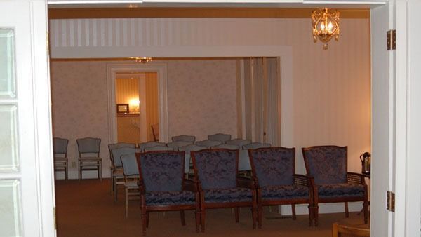 A view of a funeral home chapel, with ornate chairs, neutral walls, and a chandelier.