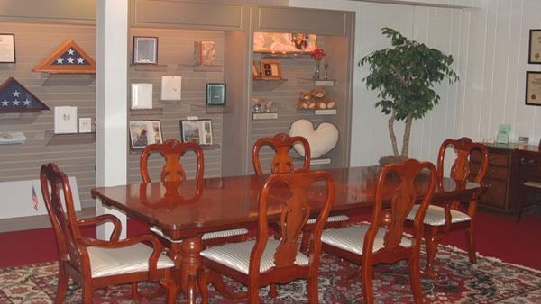 Dining room with mahogany table, ornate chairs, displays of memorial items, and a potted tree.