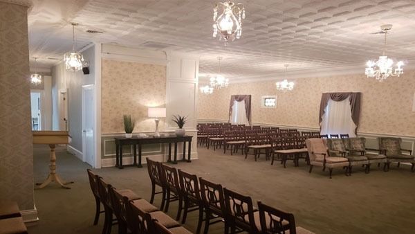 Funeral home interior with chairs arranged for a service, chandeliers, and floral wallpaper.