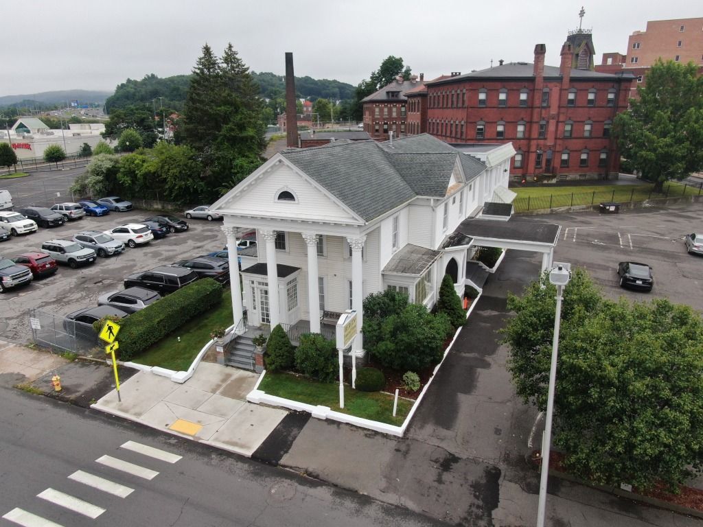 White building with columns, parking lot, and crosswalk; urban setting.