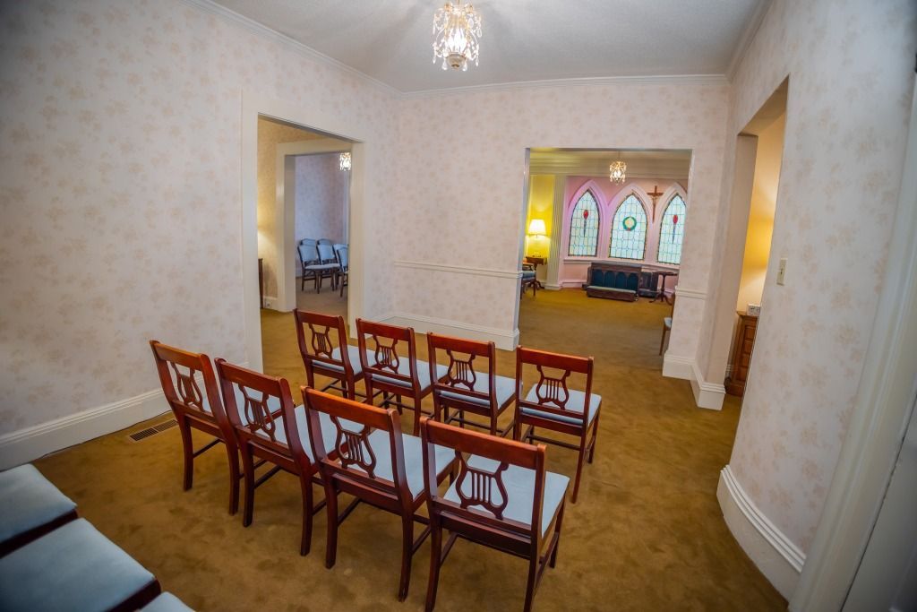 Empty room with chairs, carpet, and doorways leading to other rooms, presumably a funeral home.