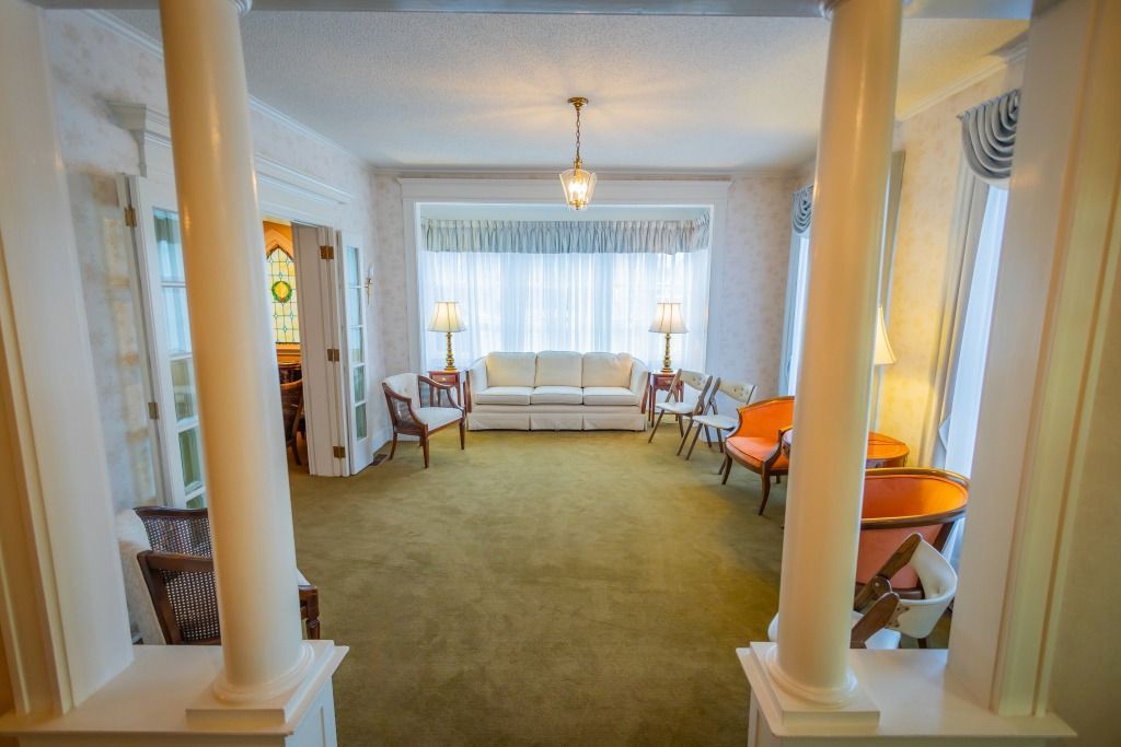 Living room with columns, sofa, chairs, lamps, and a window with white curtains.