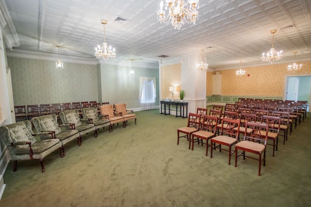 Funeral home interior with seating rows, chandeliers, and green carpet.