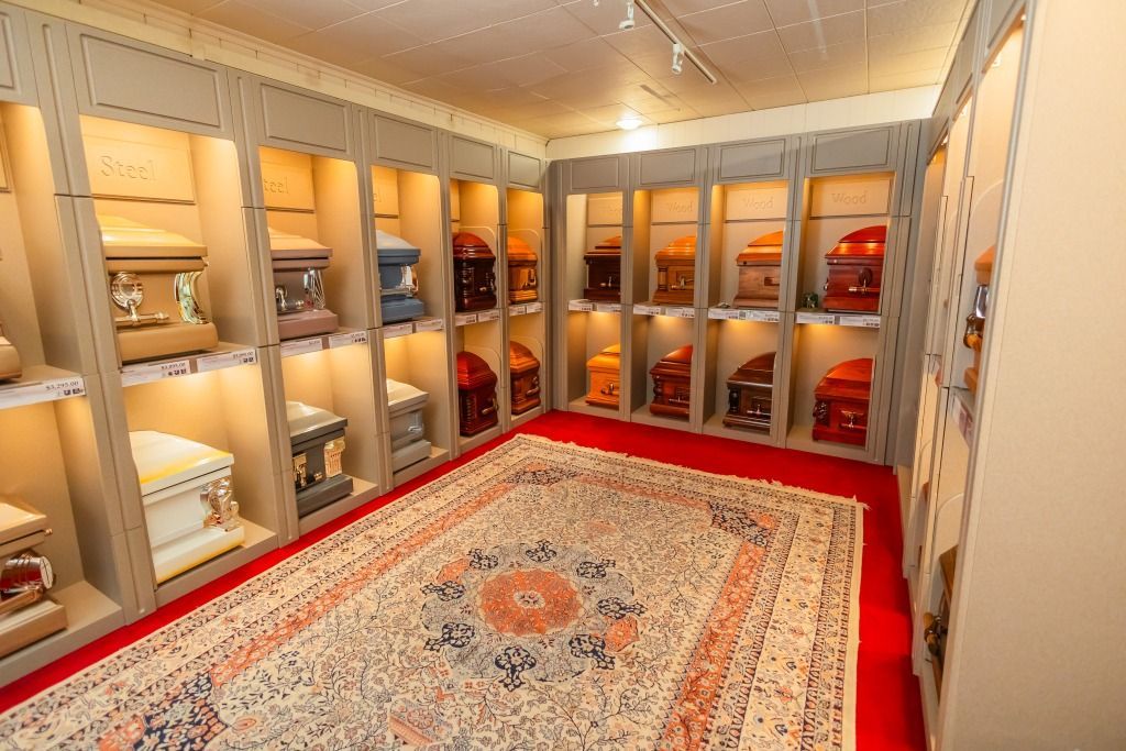 Room with shelves displaying caskets, Persian rug on red carpet. Warm lighting, museum setting.
