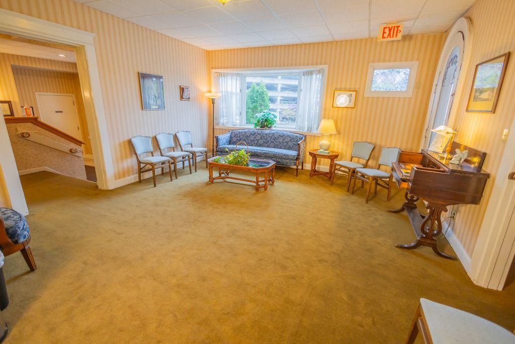 Waiting room with yellow walls, carpet, and chairs. A couch and window are present.