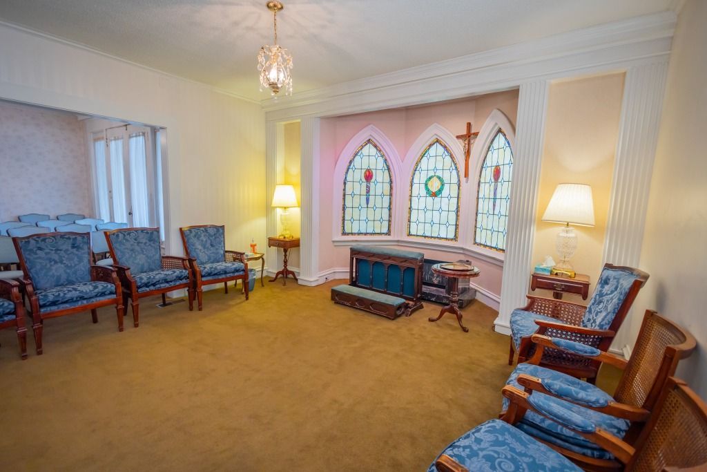 Interior of a funeral home chapel with chairs, stained glass windows, and a cross.