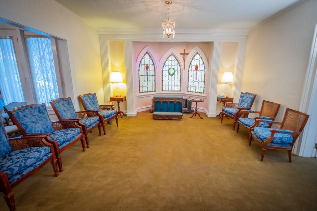 Interior of a chapel with blue chairs arranged in a circle, stained-glass windows, and a carpeted floor.