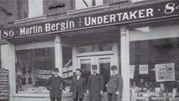 Exterior of Martin Bergin Undertaker's shop with employees standing in front. Sign above door. Black and white.