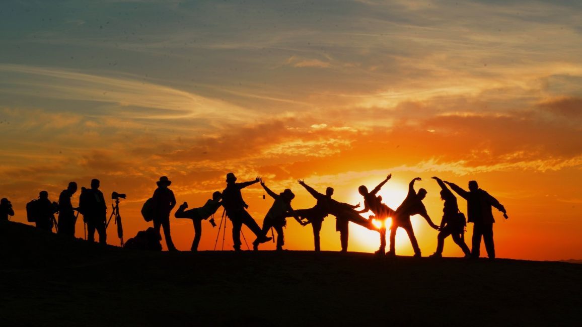 a group of people are standing in a row holding hands at sunset .