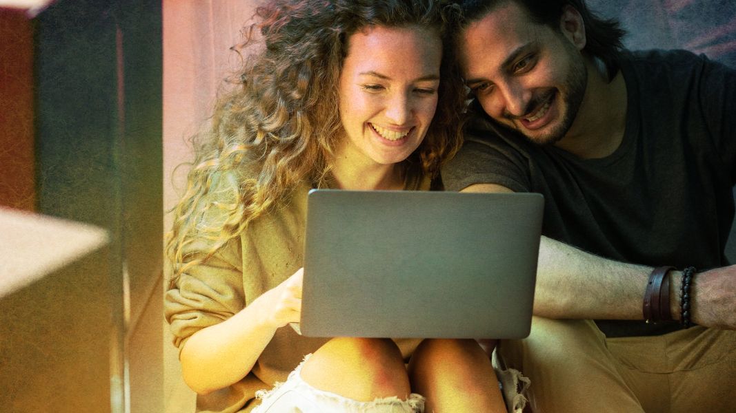 a man and a woman are smiling while looking at a laptop