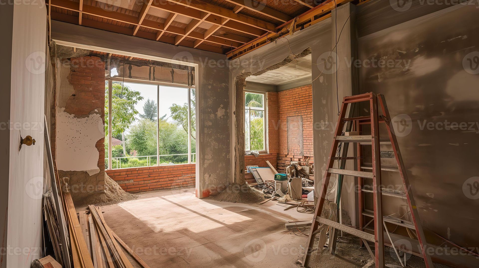 An interior room under construction with exposed brick walls, a wooden ladder, and large windows overlooking trees.