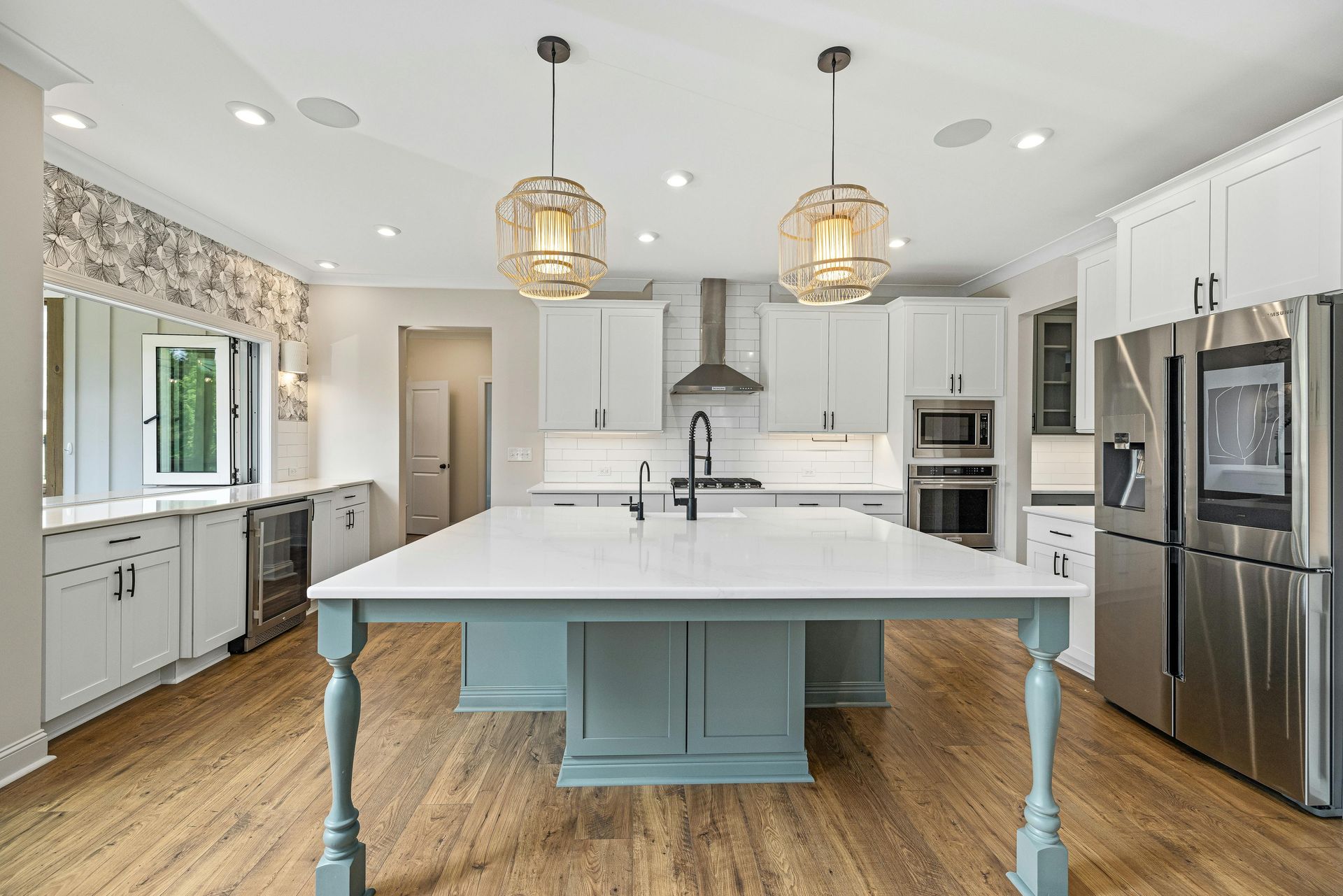 A bright kitchen with a light blue central island, white cabinetry, stainless steel appliances, and wood-look flooring.