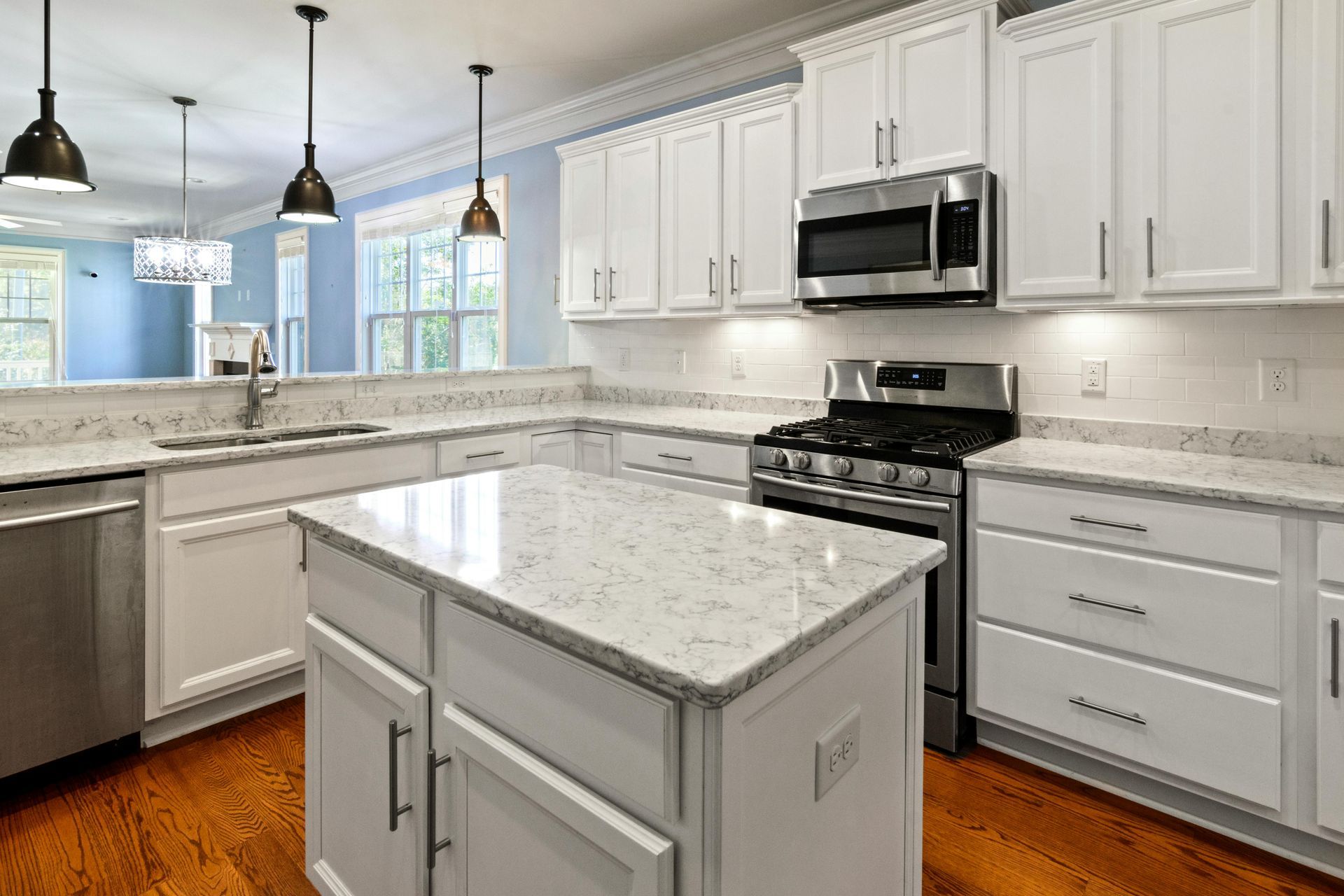 A modern white kitchen with a granite island, stainless steel appliances, and hardwood floors.