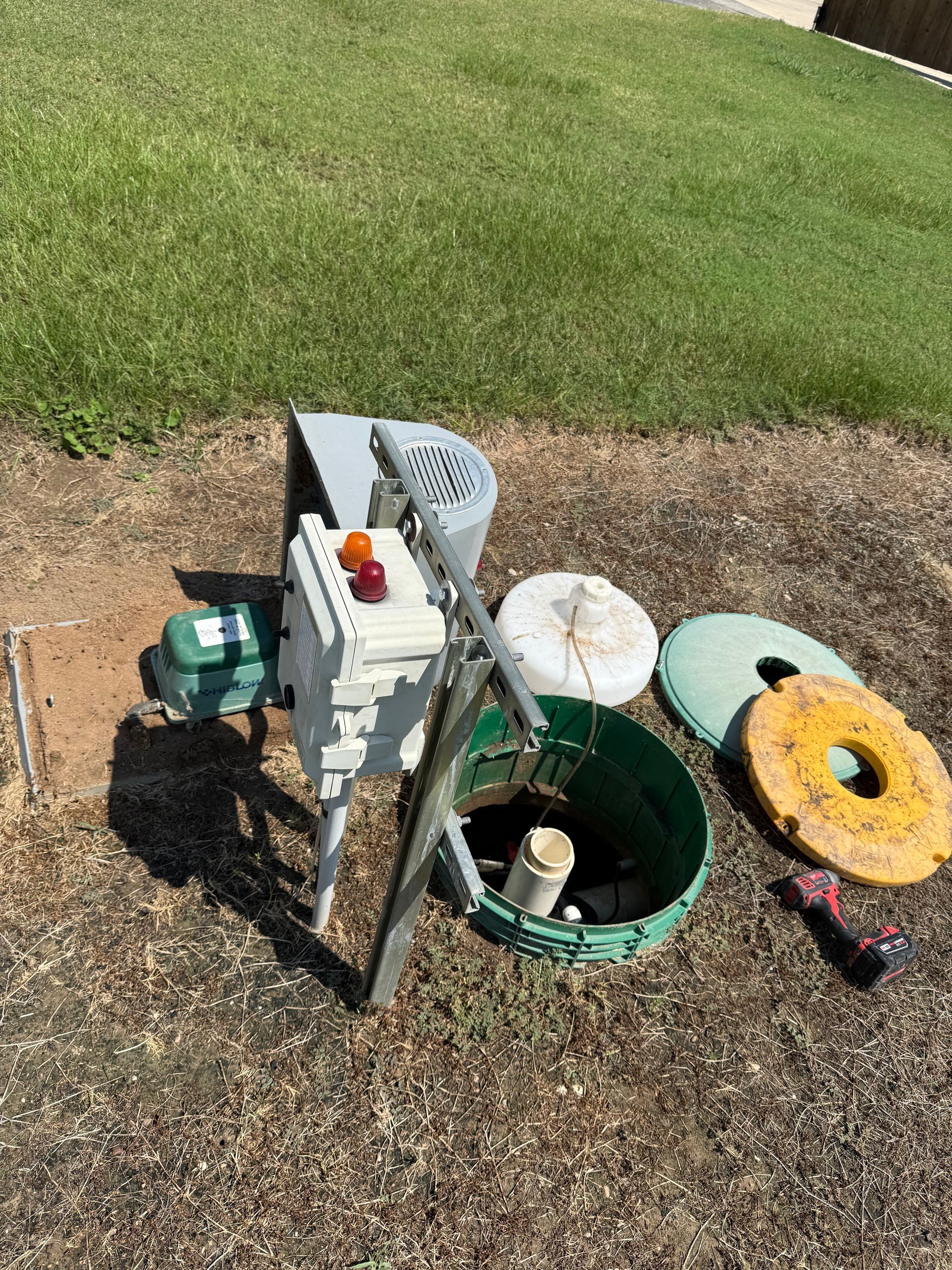 Garden tools and supplies beside a green utility hole cover on a lawn edge