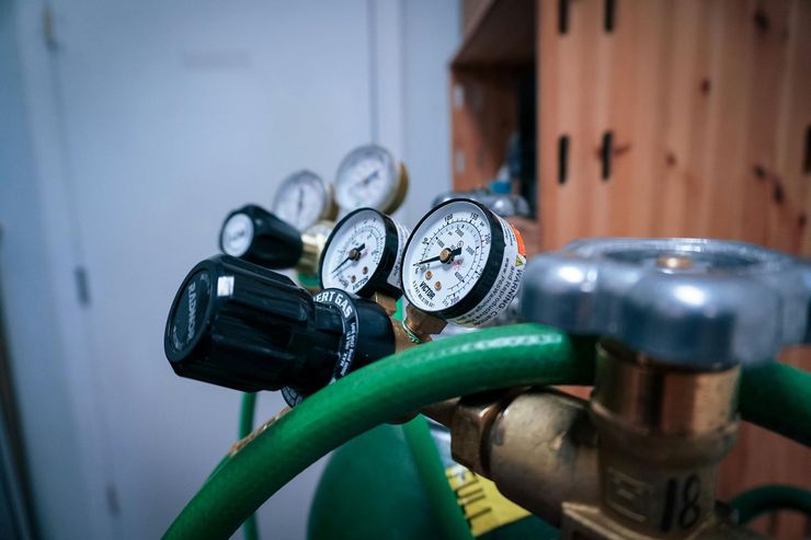 Close-up of pressure gauges and green hose on a gas tank regulator indoors