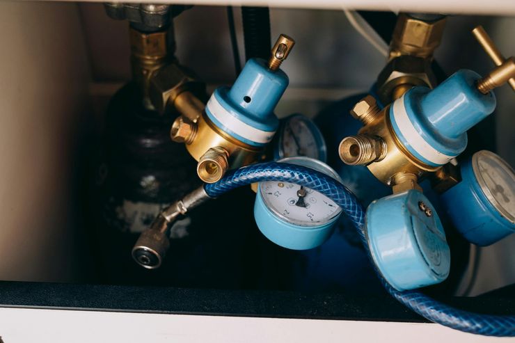 Blue gas regulator valves attached to pipes in a dark utility area