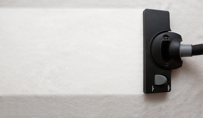 Una aspiradora está limpiando una manta blanca sobre una cama.