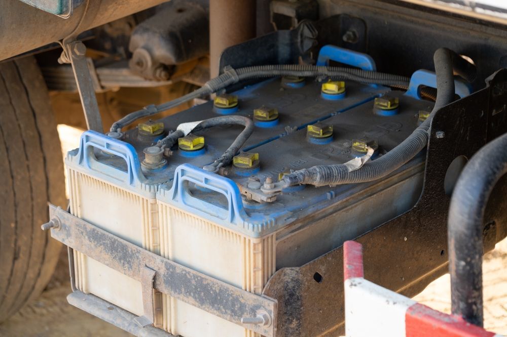 Two truck batteries, side-by-side, are connected. The batteries are black with yellow and blue details, mounted on a truck.