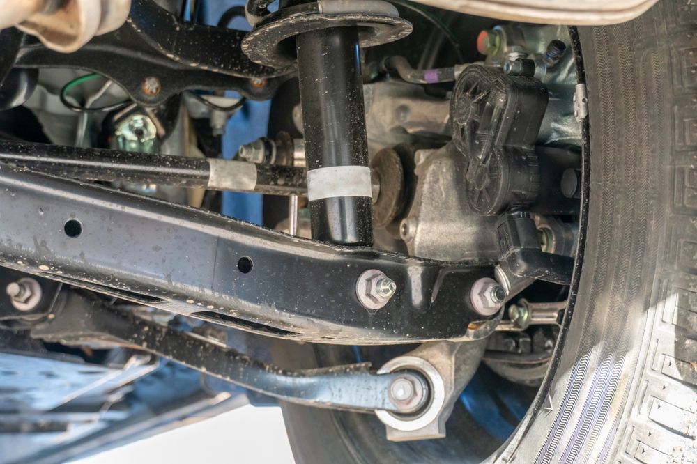 Car's rear suspension components, including shock absorber, control arms, and tire sidewall.