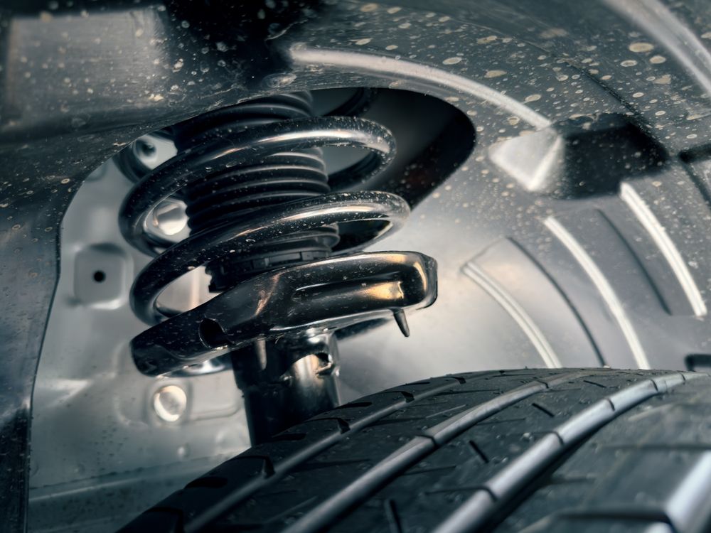 Car suspension system: shock absorber with coil spring, mounted above a tire.