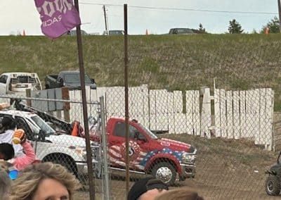 Red truck with American flag graphics parked near white fence and crowd.
