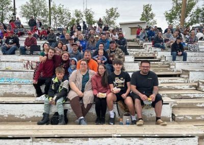 Large group of people sitting on concrete bleachers outdoors, smiling for a group photo.