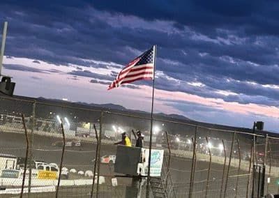 American flag waving at a racetrack, sunset sky.