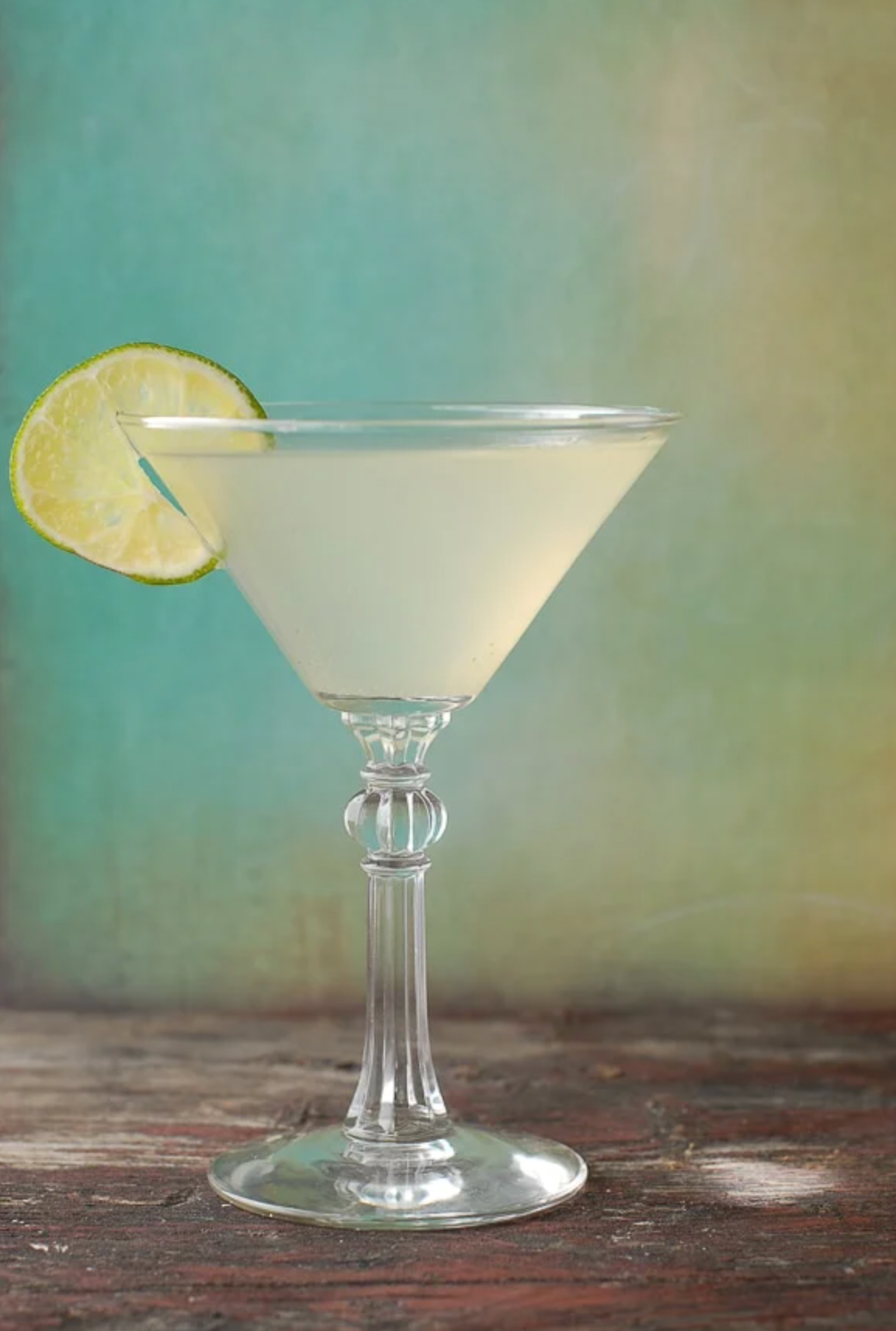 A martini glass with a slice of lime on a wooden table.