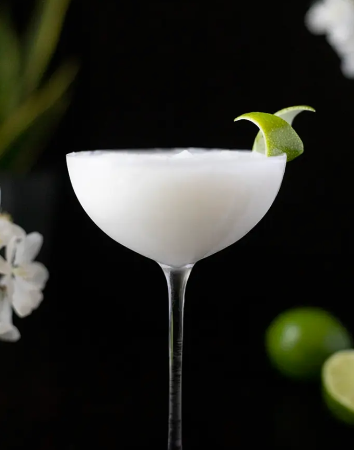 A white cocktail in a martini glass with a lime wedge on top.