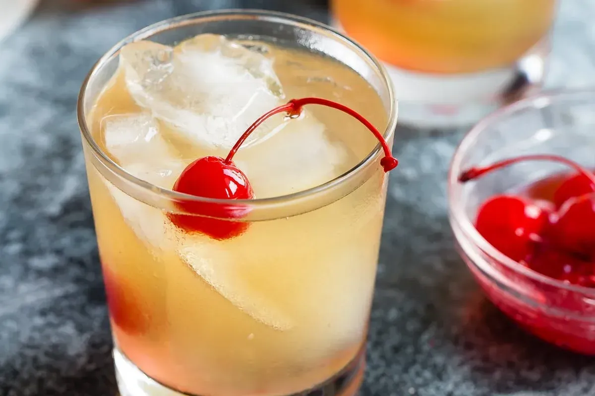 A close up of a drink with ice and a cherry on top.