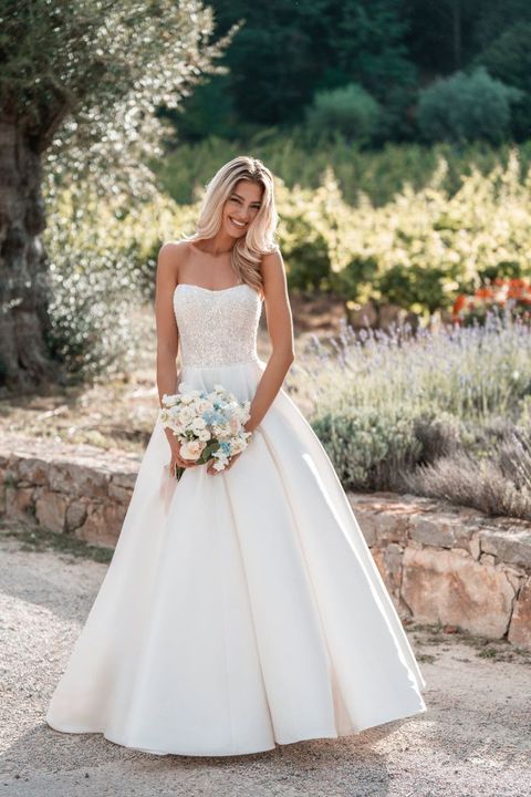 The bride is wearing a strapless wedding dress and holding a bouquet of flowers.