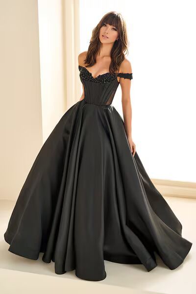 A woman in a black ball gown is standing in front of a window.