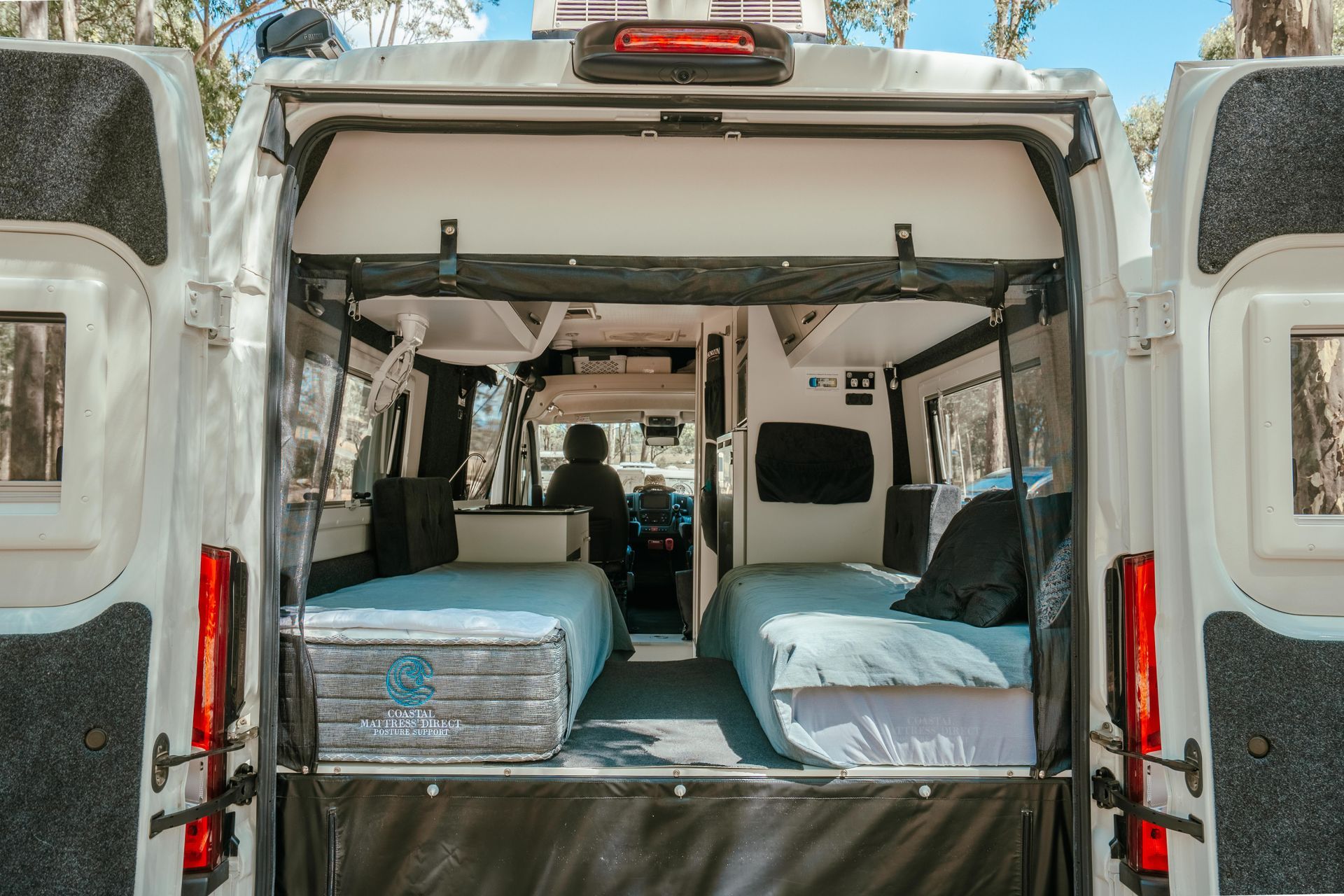 Open van with two beds inside, white walls, and a person in the driver's seat.
