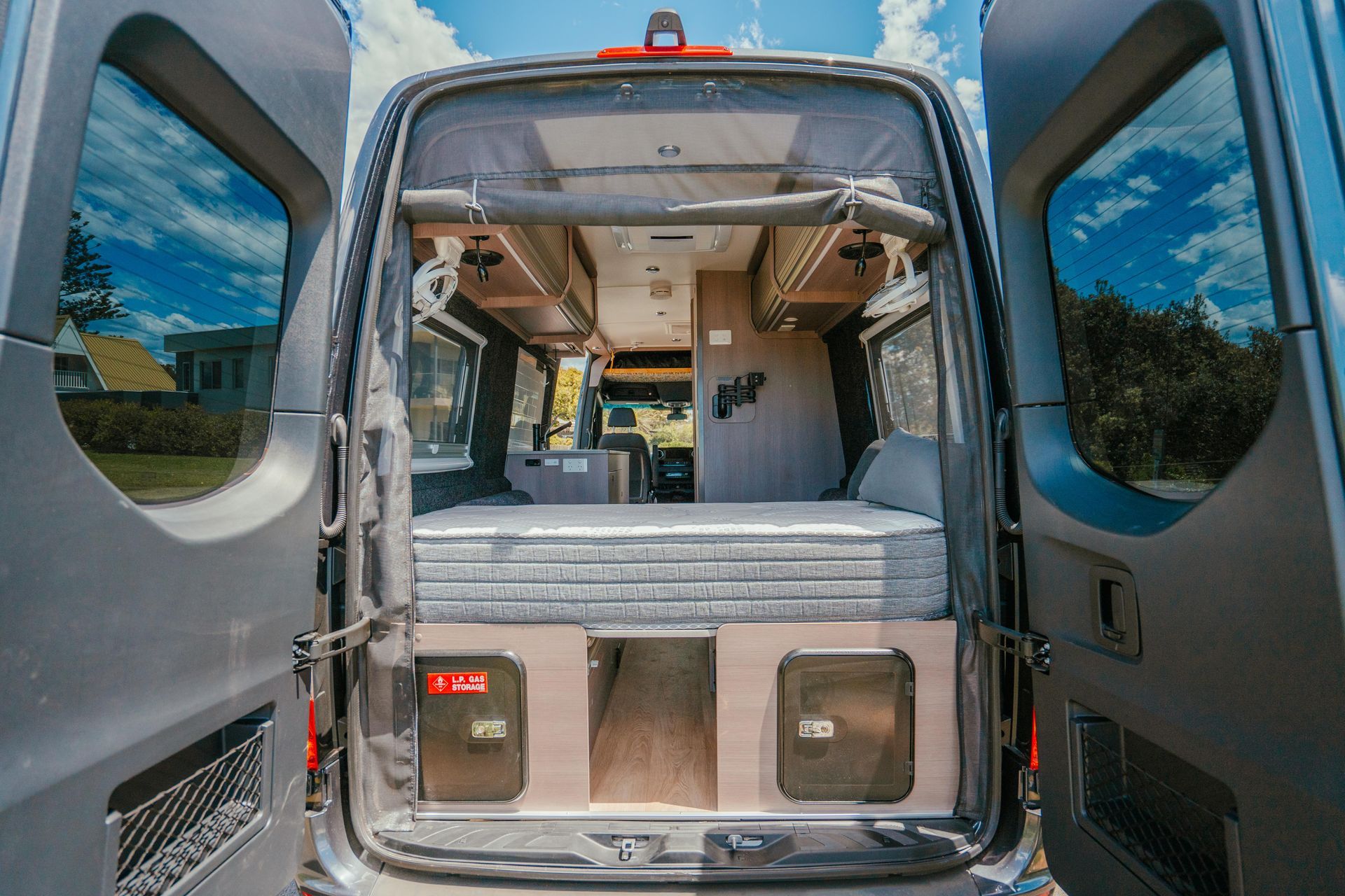 Open rear doors of a camper van reveal a bed, storage, and interior living space.