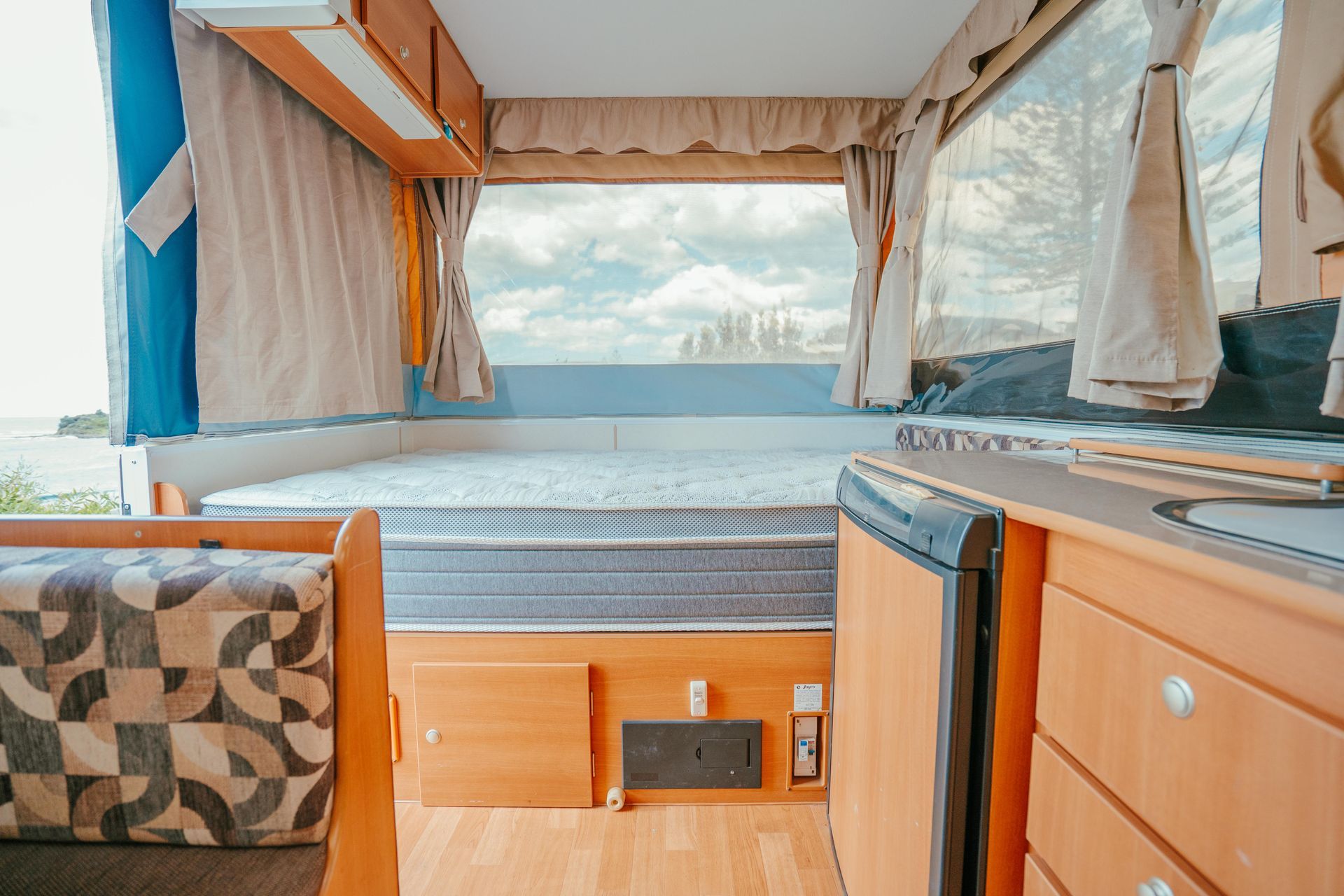 Interior of a camper with a bed, small kitchen, and a large window overlooking a scenic view — Coastal Mattress' Direct in South Nowra, NSW