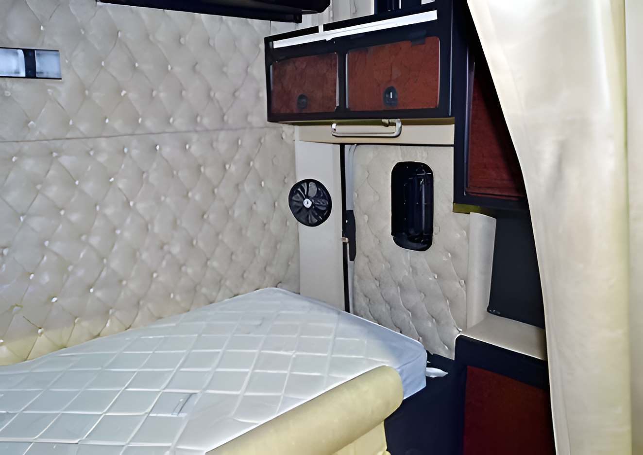 Interior of a pop-up camper with a bed, window, curtains, and wooden cabinets.