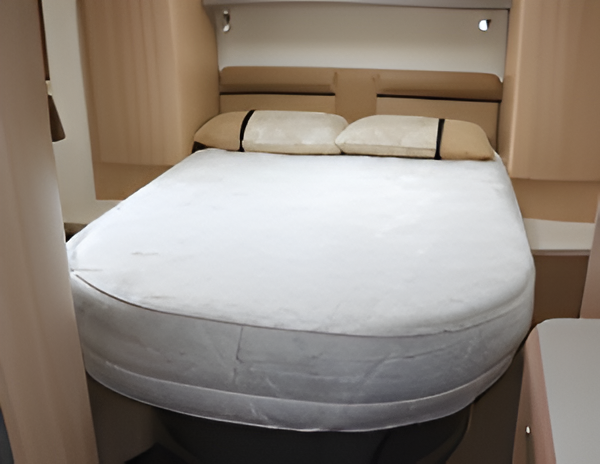 A bed in a motorhome. It has a rounded mattress, headboard, and two pillows.