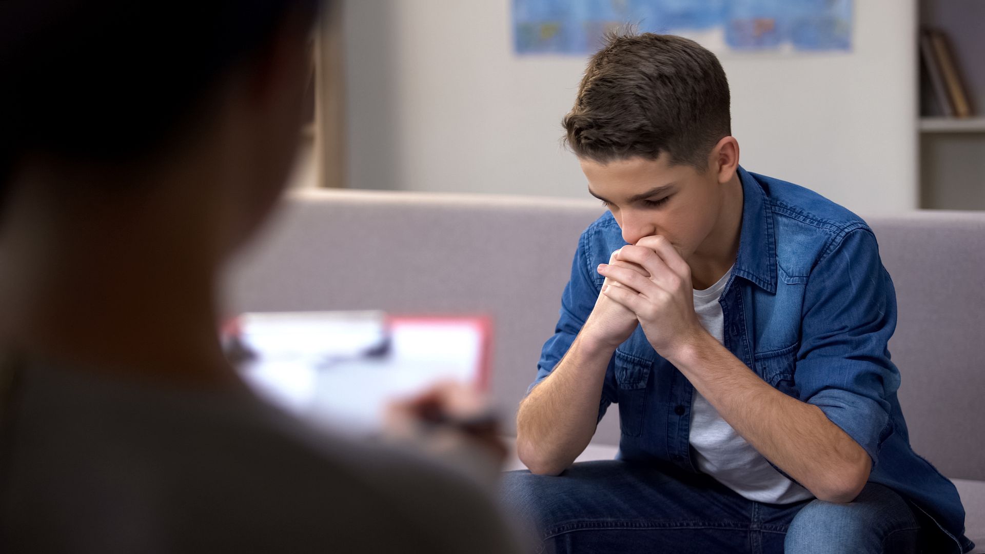 A young man is sitting on a couch talking to a woman.