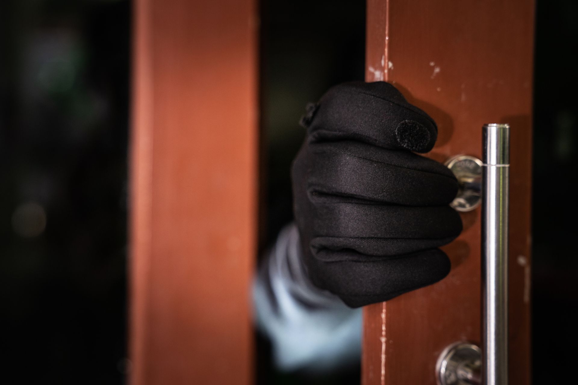 A person wearing black gloves is holding a door handle.