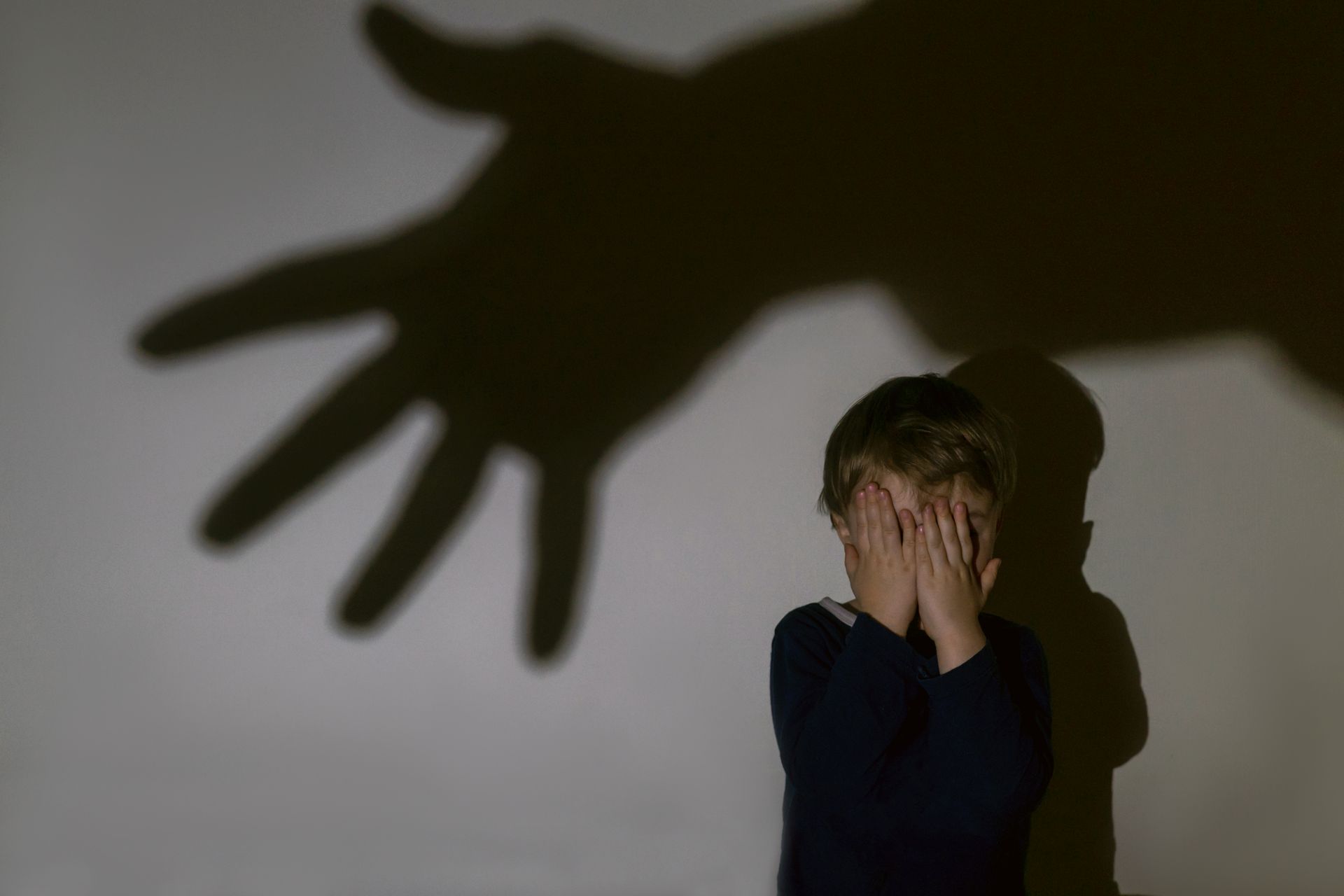 A young boy is covering his face in front of a shadow of a hand.