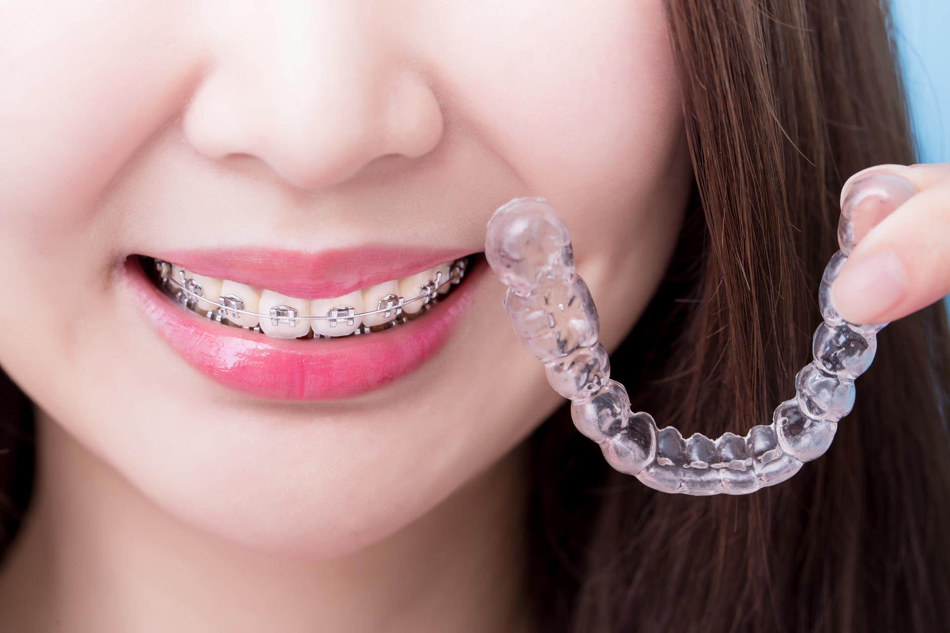 woman with braces on smiling and holding invisalign clear aligners | coraopolis PA