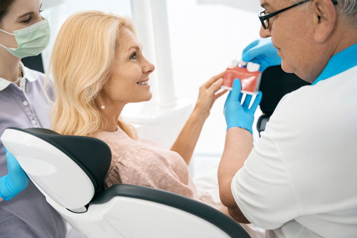 A woman is sitting in a dental chair while a dentist shows her a model of her teeth.