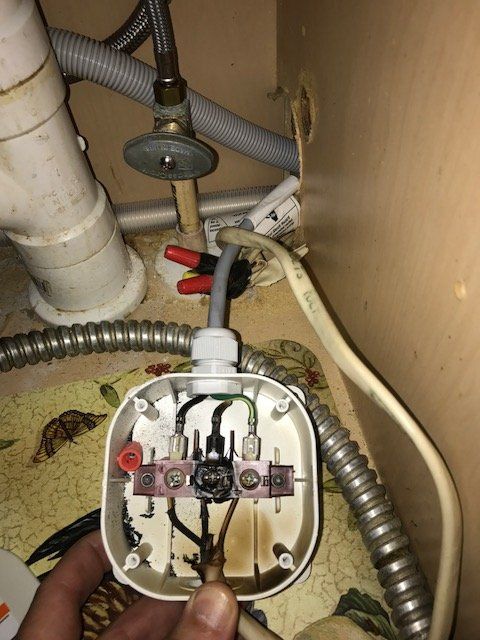 A person is holding a plug under a sink.