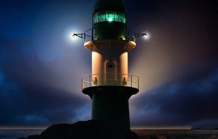 A lighthouse is lit up at night in the middle of the ocean