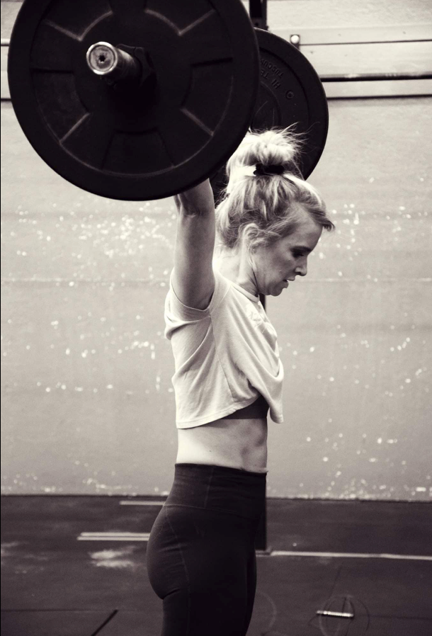 A woman is lifting a barbell over her head in a gym.